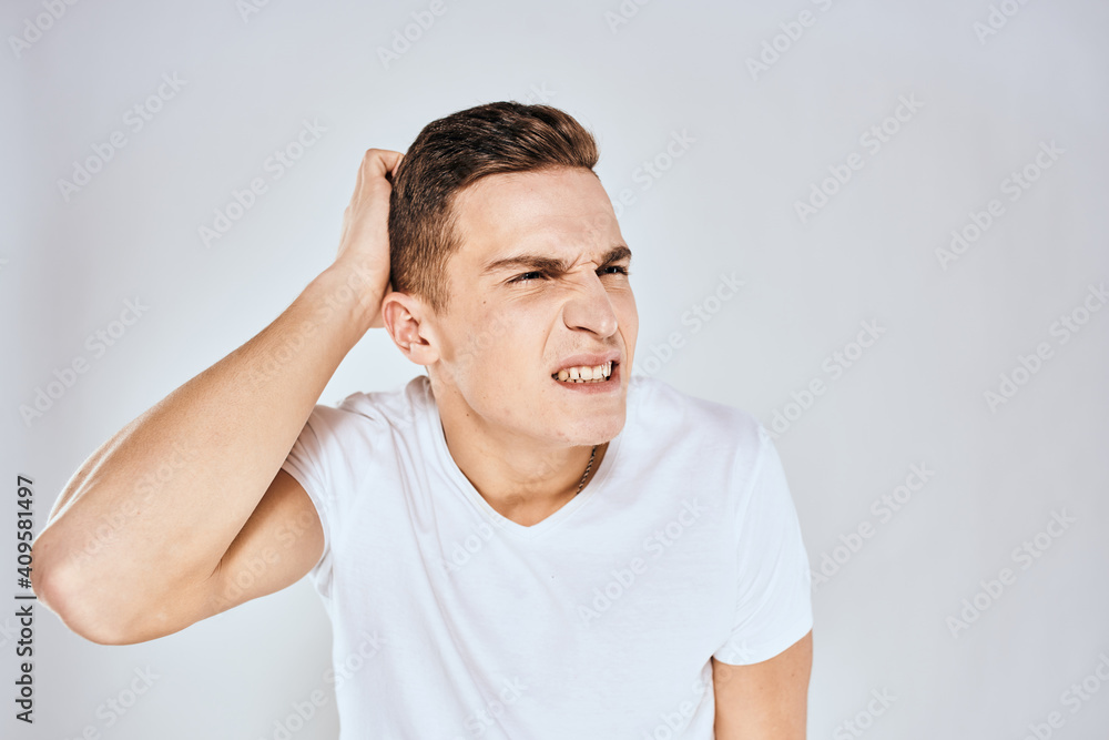 Obraz premium Emotional man in a white t-shirt holds his hand on his face light background