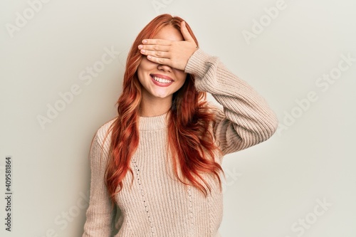 Young beautiful redhead woman wearing casual winter sweater smiling and laughing with hand on face covering eyes for surprise. blind concept.