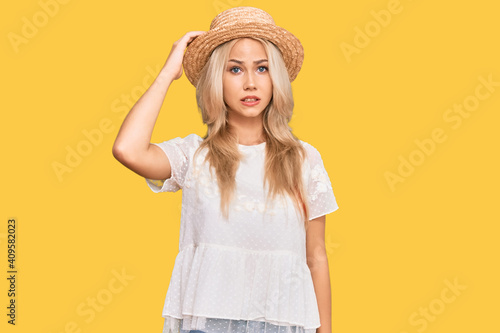Young blonde girl wearing summer hat confuse and wonder about question. uncertain with doubt, thinking with hand on head. pensive concept.