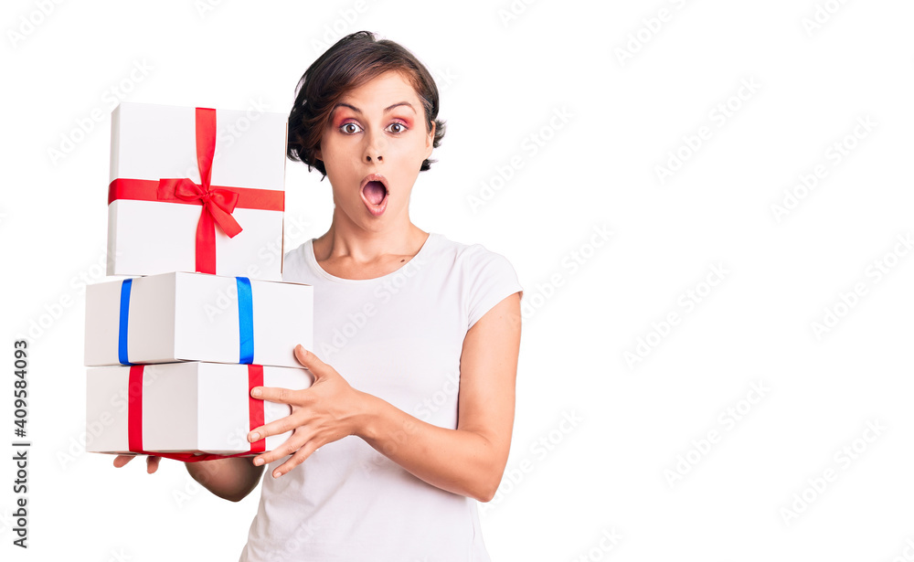 Beautiful young woman with short hair holding gifts scared and amazed with open mouth for surprise, disbelief face Beautiful young woman with short hair holding gifts scared and amazed with open mouth for surprise, disbelief face