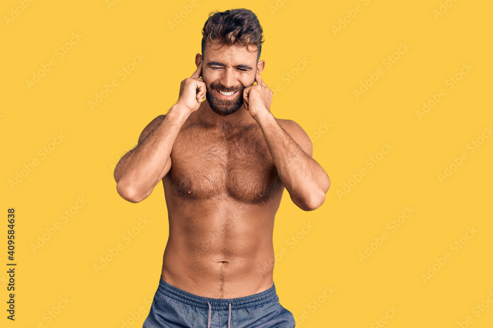 Fototapeta premium Young hispanic man wearing swimwear shirtless covering ears with fingers with annoyed expression for the noise of loud music. deaf concept.