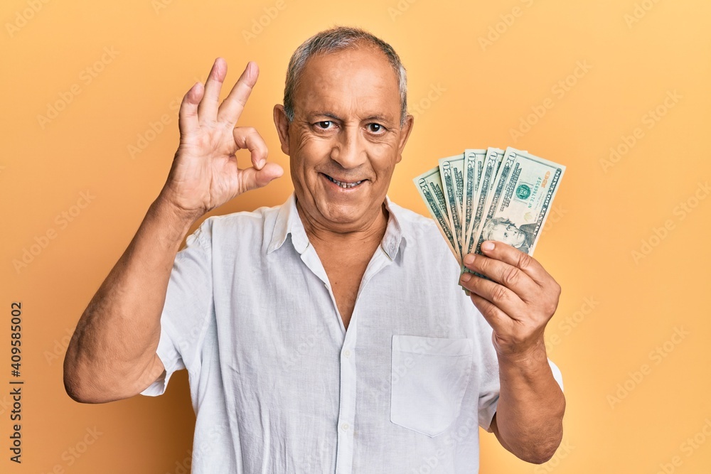 Handsome mature man holding 20 dollars banknotes doing ok sign with fingers, smiling friendly gesturing excellent symbol Handsome mature man holding 20 dollars banknotes doing ok sign with fingers, smiling friendly gesturing excellent symbol