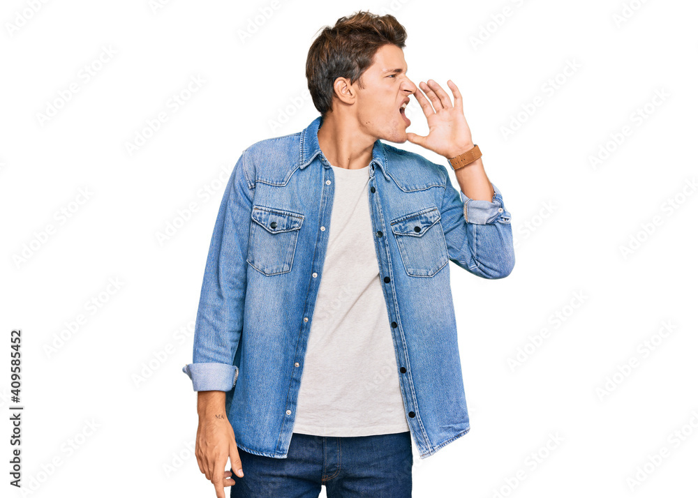 Handsome caucasian man wearing casual denim jacket shouting and screaming loud to side with hand on mouth. communication concept. Handsome caucasian man wearing casual denim jacket shouting and screaming loud to side with hand on mouth. communication concept.