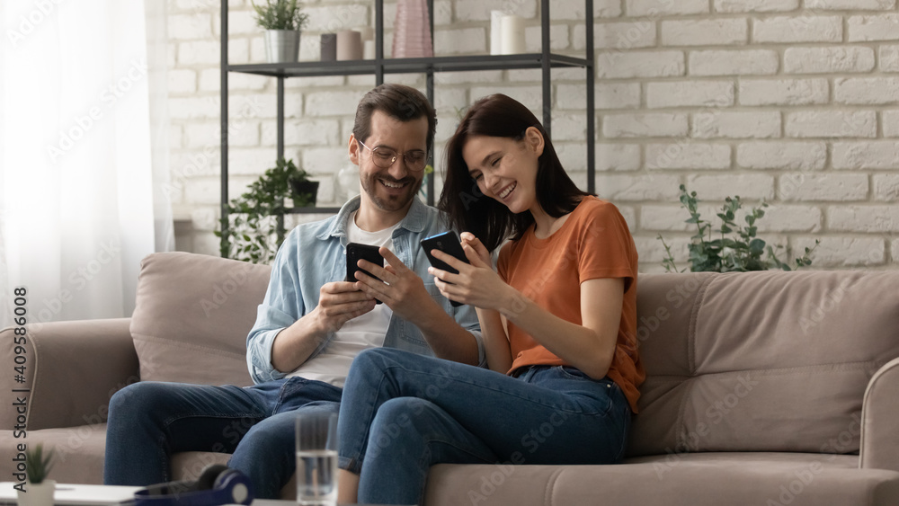 Overjoyed couple using phones together, sitting on cozy couch at home, happy man wearing glasses and woman surfing internet, holding smartphones, having fun with gadgets, enjoying leisure time Overjoyed couple using phones together, sitting on cozy couch at home, happy man wearing glasses and woman surfing internet, holding smartphones, having fun with gadgets, enjoying leisure time