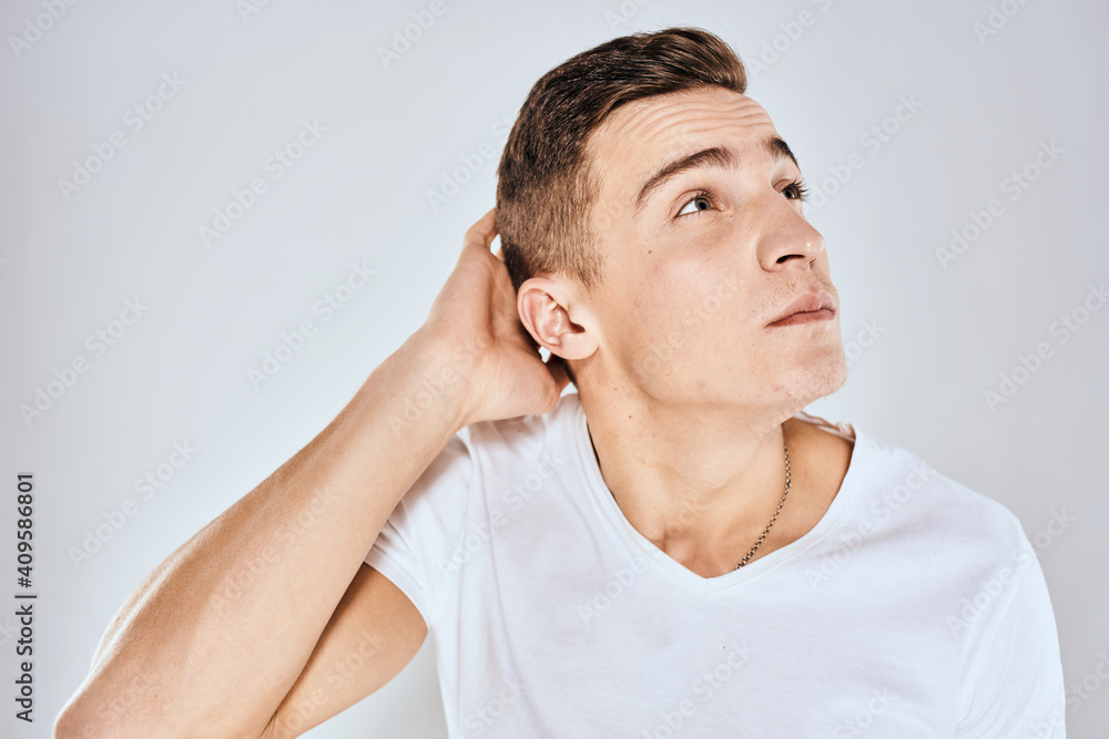 Emotional man in a white t-shirt holds his hand on his face light background Emotional man in a white t-shirt holds his hand on his face light background