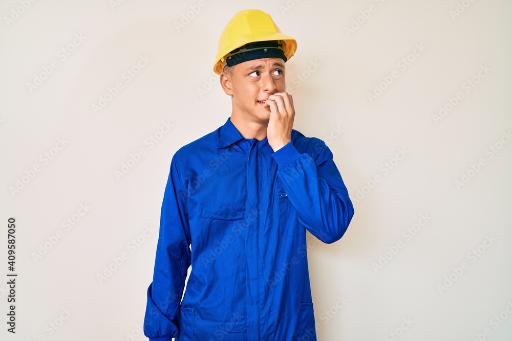 Young hispanic boy wearing worker uniform and hardhat looking stressed and nervous with hands on mouth biting nails. anxiety problem.