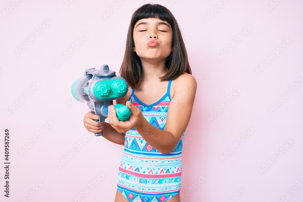 Young little girl with bang wearing swimsuit and watergun looking at the camera blowing a kiss being lovely and sexy. love expression. Young little girl with bang wearing swimsuit and watergun looking at the camera blowing a kiss being lovely and sexy. love expression.