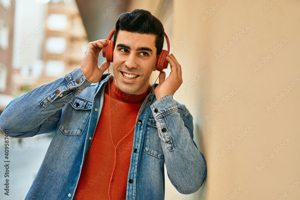 Young hispanic man smiling happy using headphones at the city. Young hispanic man smiling happy using headphones at the city.