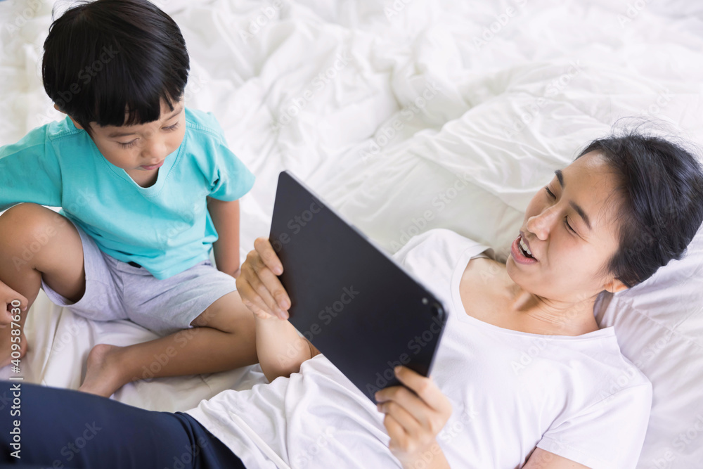 mother and her son using digital tablet in a bed at home. The use of concept of new generation, family, parenthood, authenticity, connection, technology. mother and her son using digital tablet in a bed at home. The use of concept of new generation, family, parenthood, authenticity, connection, technology.