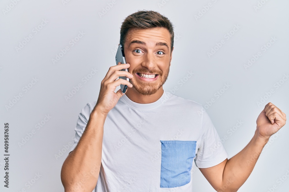 Handsome caucasian man having conversation talking on the smartphone screaming proud, celebrating victory and success very excited with raised arm Handsome caucasian man having conversation talking on the smartphone screaming proud, celebrating victory and success very excited with raised arm