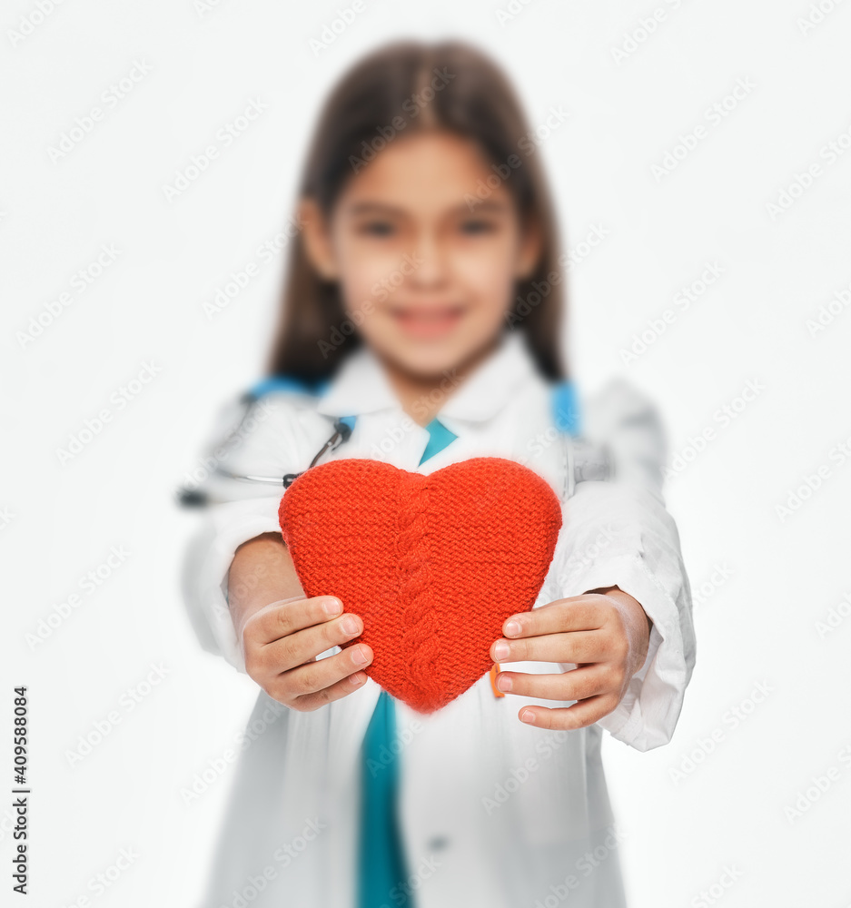 Female kid wearing a medical coat holding shape of a heart in front of her. Child heart health concept. Soft focus Female kid wearing a medical coat holding shape of a heart in front of her. Child heart health concept. Soft focus