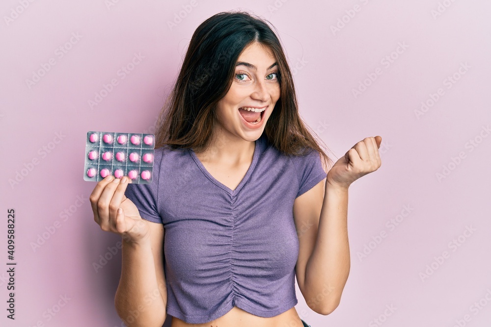 Young caucasian woman holding pills screaming proud, celebrating victory and success very excited with raised arm Young caucasian woman holding pills screaming proud, celebrating victory and success very excited with raised arm
