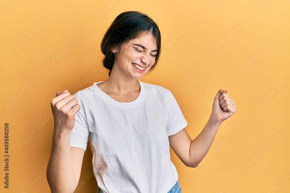 Young caucasian woman wearing casual white t shirt very happy and excited doing winner gesture with arms raised, smiling and screaming for success. celebration concept. Young caucasian woman wearing casual white t shirt very happy and excited doing winner gesture with arms raised, smiling and screaming for success. celebration concept.