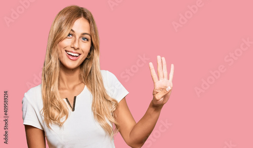 Beautiful blonde young woman wearing casual white tshirt showing and pointing up with fingers number four while smiling confident and happy.