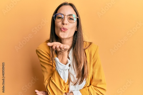 Young beautiful woman wearing business style and glasses looking at the camera blowing a kiss with hand on air being lovely and sexy. love expression.
