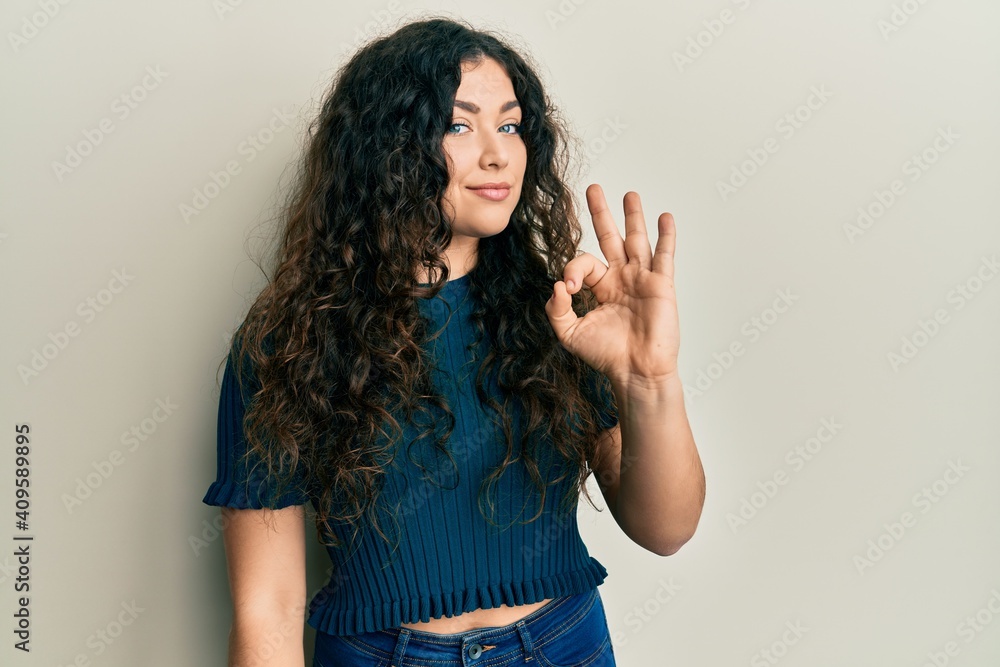 Young brunette woman with curly hair wearing casual clothes smiling positive doing ok sign with hand and fingers. successful expression. Young brunette woman with curly hair wearing casual clothes smiling positive doing ok sign with hand and fingers. successful expression.
