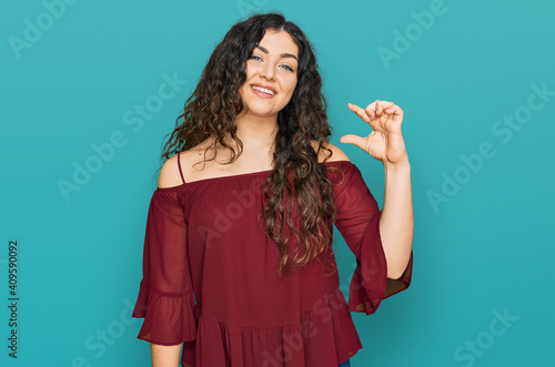 Young hispanic girl wearing casual clothes smiling and confident gesturing with hand doing small size sign with fingers looking and the camera. measure concept.