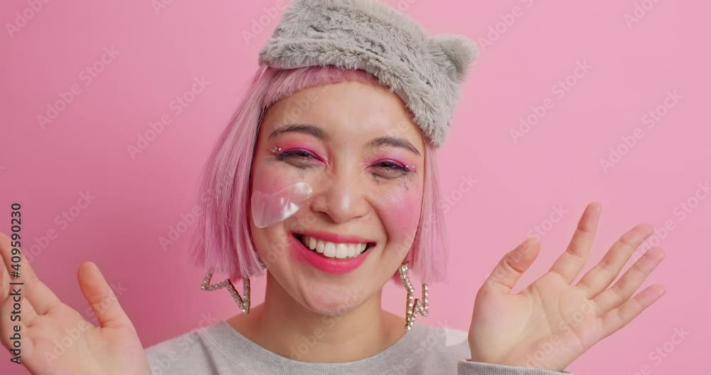 Happy positive young woman covers eyes and says boo reacts on something raises palms has spoiled makeup wears sleepmask isolated over pink background. People human reactions and emotions concept Happy positive young woman covers eyes and says boo reacts on something raises palms has spoiled makeup wears sleepmask isolated over pink background. People human reactions and emotions concept