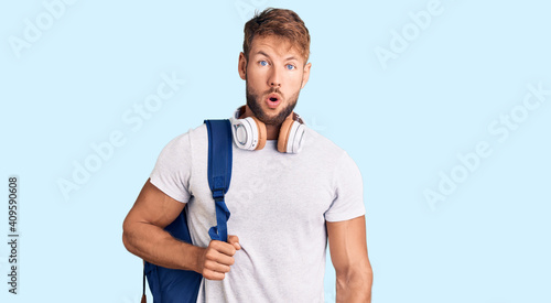 Young caucasian man wearing student backpack and headphones scared and amazed with open mouth for surprise, disbelief face