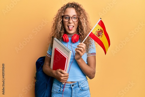 Beautiful caucasian teenager girl exchange student holding spanish flag sticking tongue out happy with funny expression. photo