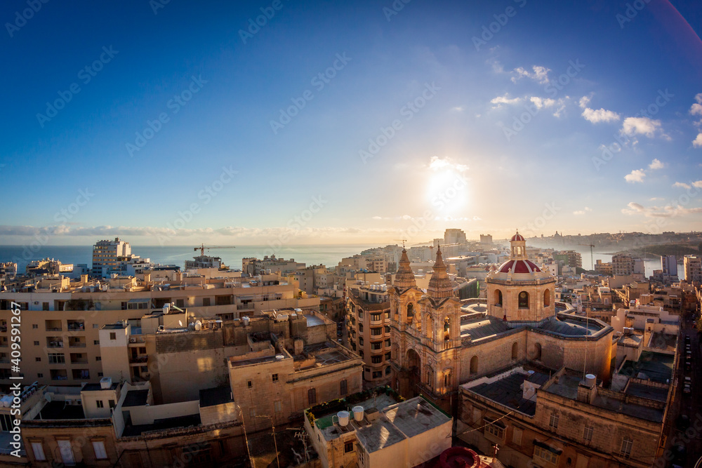 Sunrise in malta. rooftop view from sliema with a church in the foreground and blue sky and sun rising in the background
