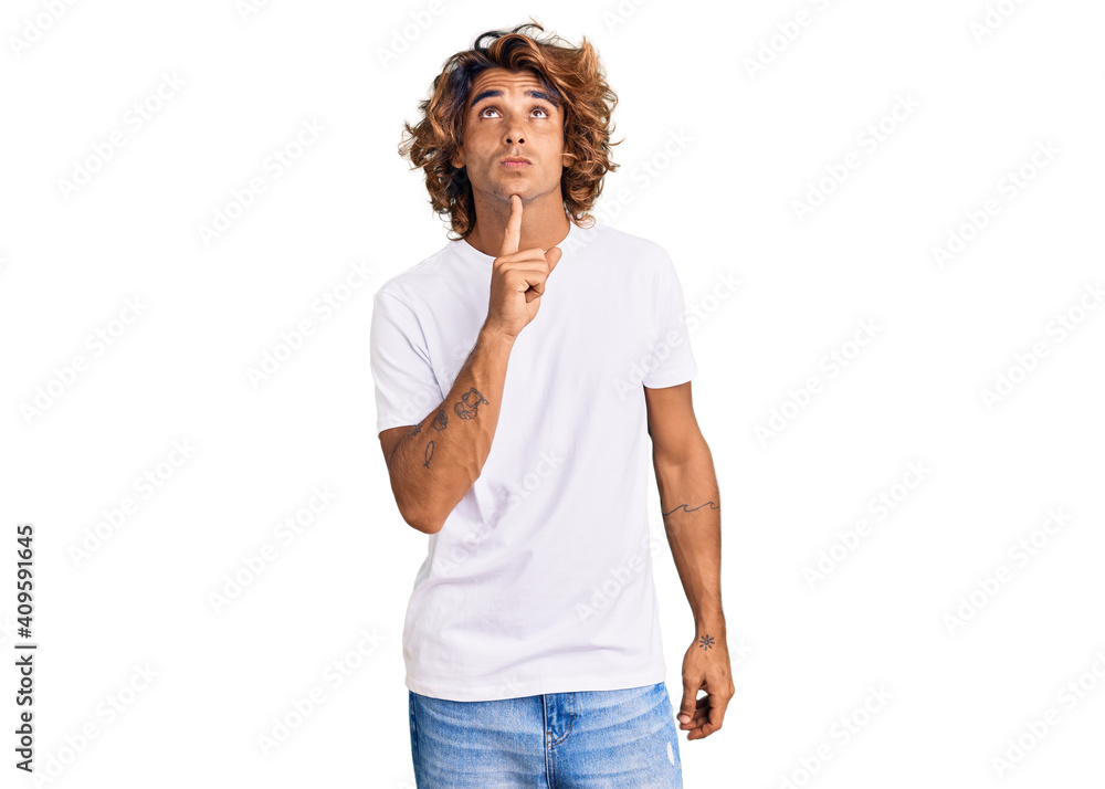 Young hispanic man wearing casual white tshirt thinking concentrated about doubt with finger on chin and looking up wondering Young hispanic man wearing casual white tshirt thinking concentrated about doubt with finger on chin and looking up wondering