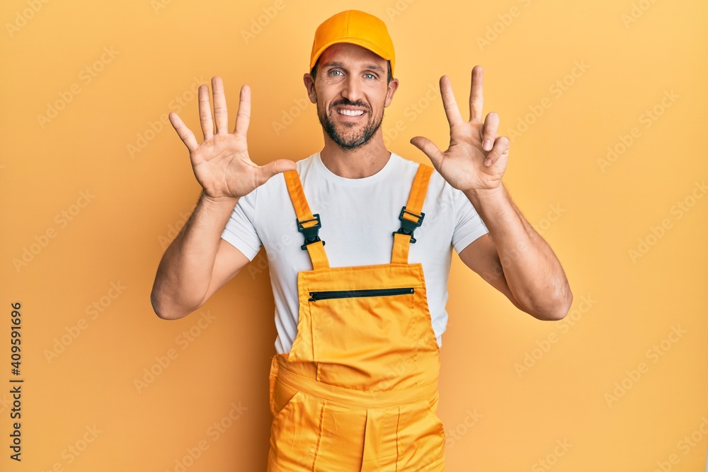 Young handsome man wearing handyman uniform over yellow background showing and pointing up with fingers number eight while smiling confident and happy.