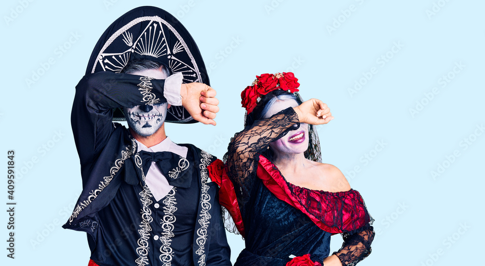 Young couple wearing mexican day of the dead costume over background covering eyes with arm smiling cheerful and funny. blind concept. Young couple wearing mexican day of the dead costume over background covering eyes with arm smiling cheerful and funny. blind concept.