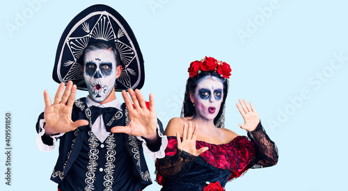 Young couple wearing mexican day of the dead costume over background doing stop gesture with hands palms, angry and frustration expression
