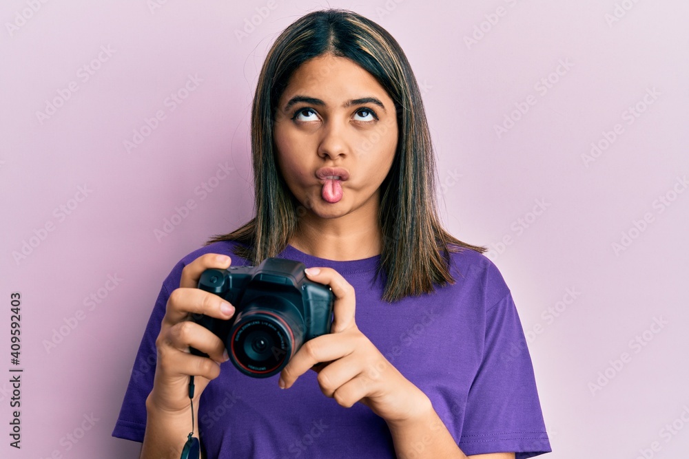 Young latin woman using reflex camera making fish face with mouth and squinting eyes, crazy and comical. Young latin woman using reflex camera making fish face with mouth and squinting eyes, crazy and comical.