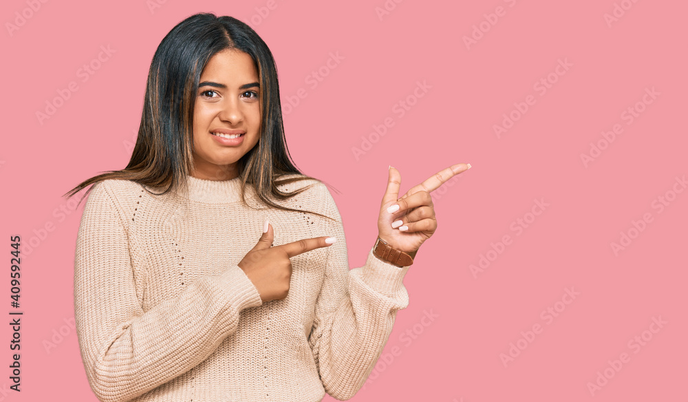 Young latin girl wearing wool winter sweater pointing aside worried and nervous with both hands, concerned and surprised expression Young latin girl wearing wool winter sweater pointing aside worried and nervous with both hands, concerned and surprised expression