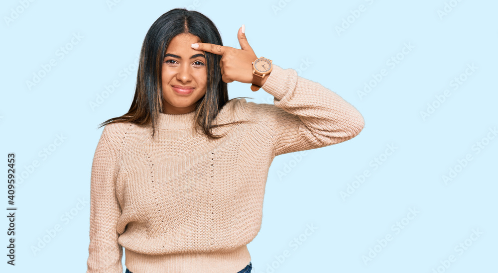 Young latin girl wearing wool winter sweater pointing unhappy to pimple on forehead, ugly infection of blackhead. acne and skin problem Young latin girl wearing wool winter sweater pointing unhappy to pimple on forehead, ugly infection of blackhead. acne and skin problem