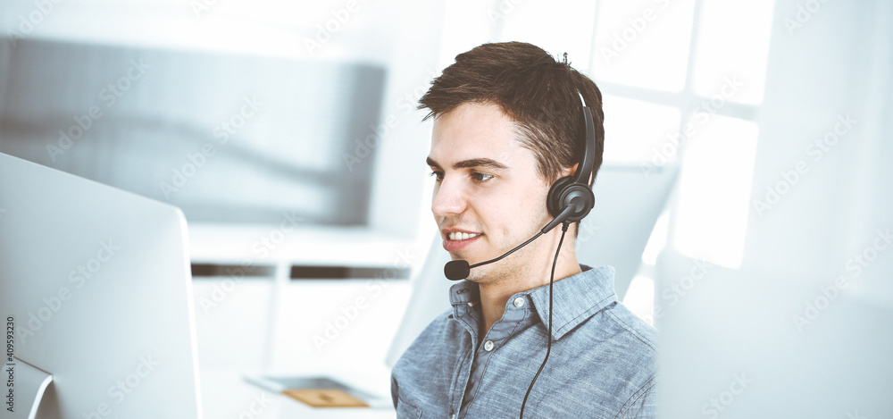 Casual dressed young man using headset and computer while talking with customers online. Call center, business concept Casual dressed young man using headset and computer while talking with customers online. Call center, business concept