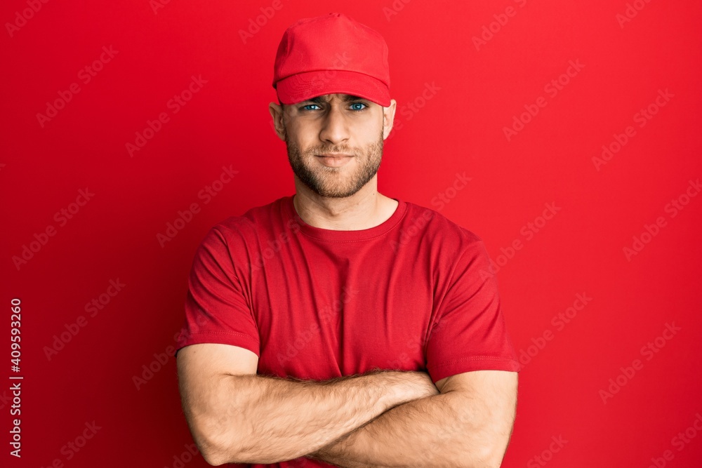 Young caucasian man wearing delivery uniform and cap skeptic and nervous, disapproving expression on face with crossed arms. negative person. Young caucasian man wearing delivery uniform and cap skeptic and nervous, disapproving expression on face with crossed arms. negative person.