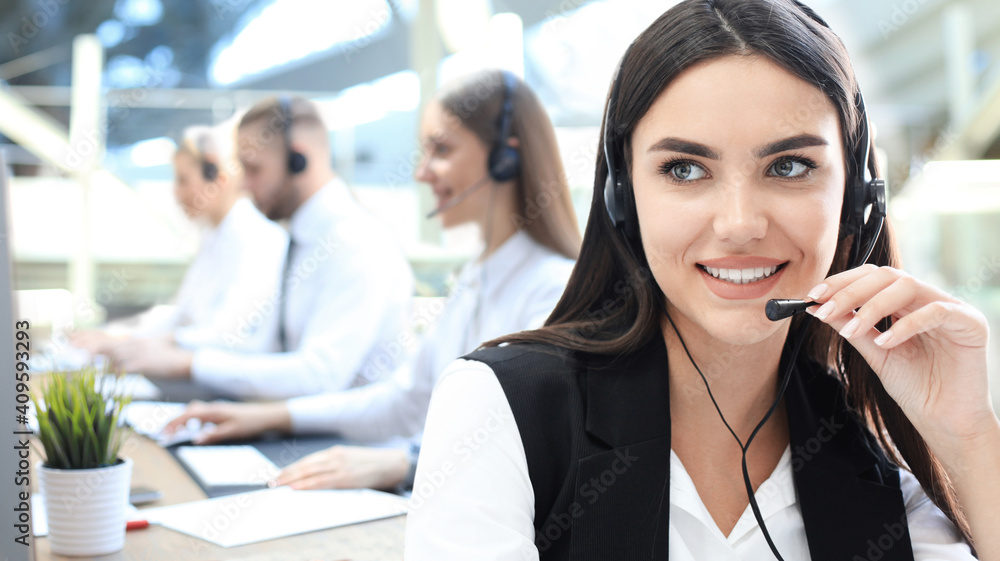 Female customer support operator with headset and smiling, with collegues at background. Female customer support operator with headset and smiling, with collegues at background.