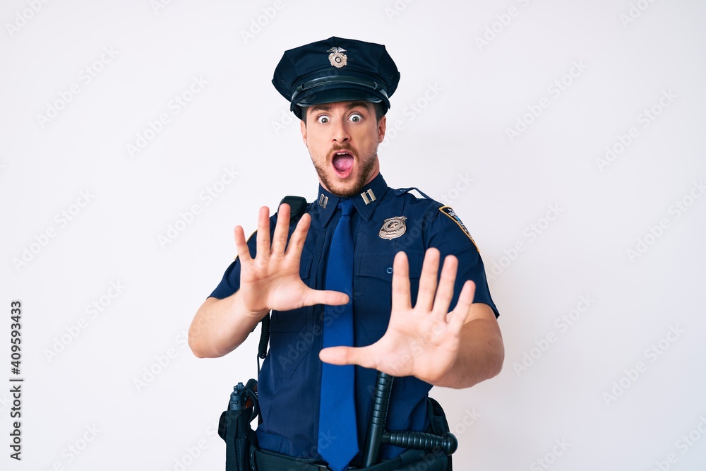 Young caucasian man wearing police uniform afraid and terrified with fear expression stop gesture with hands, shouting in shock. panic concept. Young caucasian man wearing police uniform afraid and terrified with fear expression stop gesture with hands, shouting in shock. panic concept.