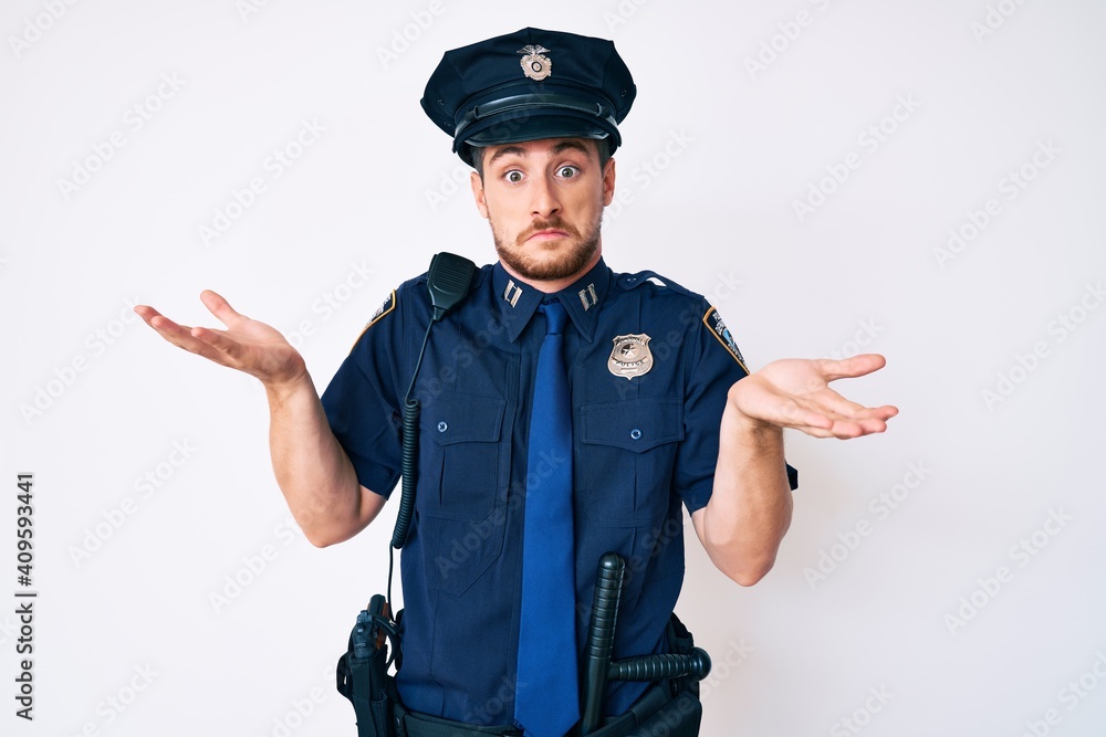 Young caucasian man wearing police uniform clueless and confused expression with arms and hands raised. doubt concept. Young caucasian man wearing police uniform clueless and confused expression with arms and hands raised. doubt concept.