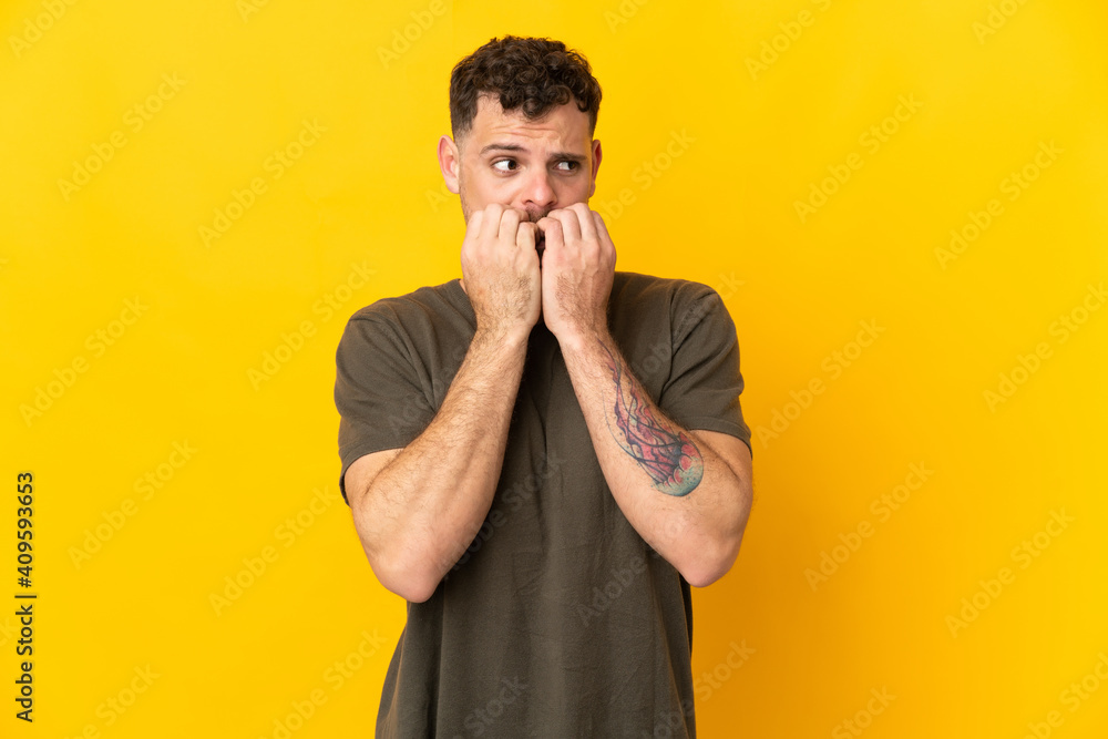 Young caucasian handsome man isolated on yellow background nervous and scared putting hands to mouth Young caucasian handsome man isolated on yellow background nervous and scared putting hands to mouth