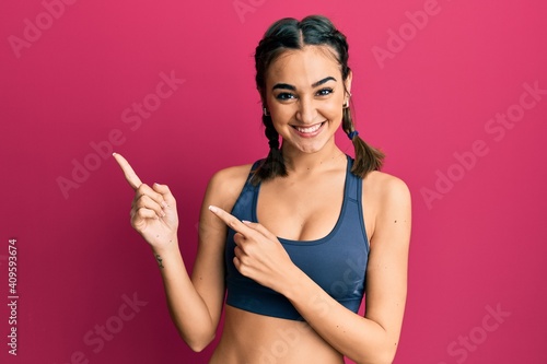 Fotografering Young brunette girl wearing sportswear and braids smiling and looking at the camera pointing with two hands and fingers to the side