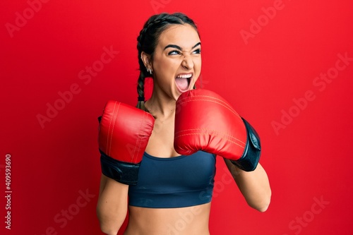 Young brunette girl using boxing gloves angry and mad screaming frustrated and furious, shouting with anger. rage and aggressive concept. © Krakenimages.com