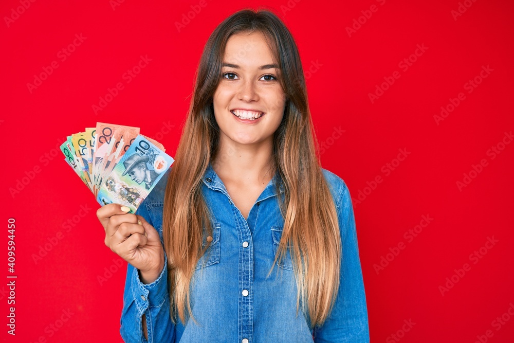 Beautiful caucasian woman holding australian dollars looking positive and happy standing and smiling with a confident smile showing teeth Beautiful caucasian woman holding australian dollars looking positive and happy standing and smiling with a confident smile showing teeth