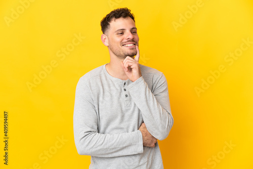 Young caucasian handsome man isolated on yellow background thinking an idea while looking up