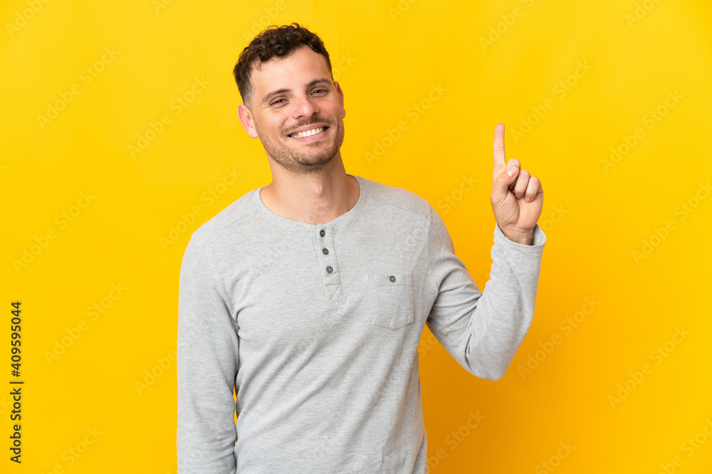 Young caucasian handsome man isolated on yellow background showing and lifting a finger in sign of the best