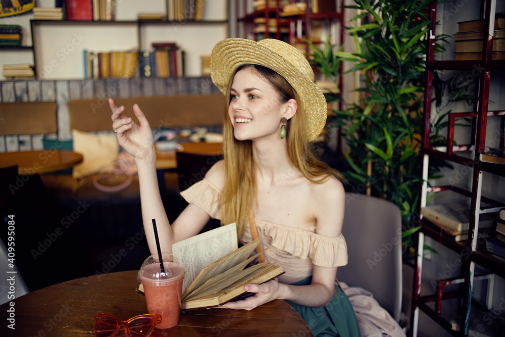 Pretty woman in hat with book in hands reading vacation in cafe