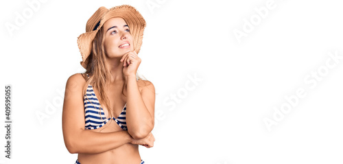 Young beautiful blonde woman wearing bikini and hat with hand on chin thinking about question, pensive expression. smiling and thoughtful face. doubt concept. photo