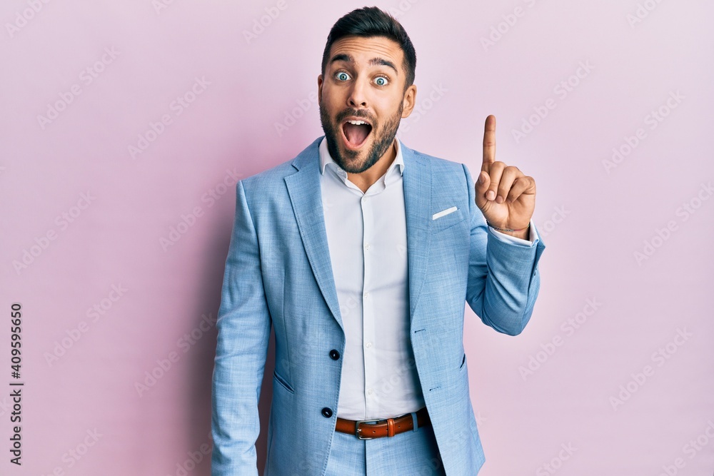 Young hispanic businessman wearing business jacket pointing finger up with successful idea. exited and happy. number one. Young hispanic businessman wearing business jacket pointing finger up with successful idea. exited and happy. number one.