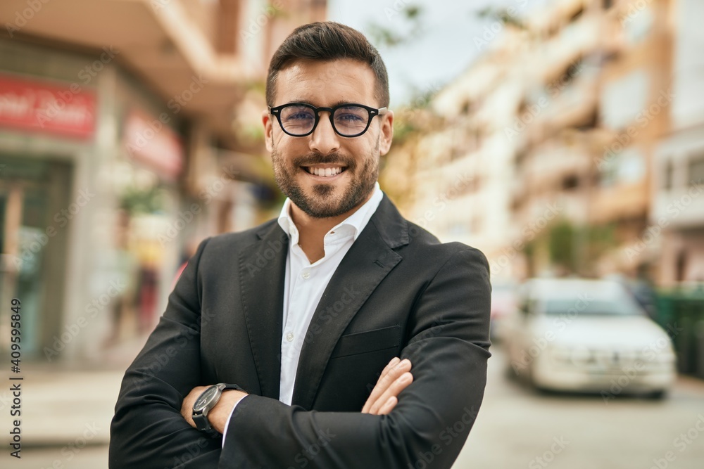 Fototapeta premium Young hispanic businessman with arms crossed smiling happy at the city.
