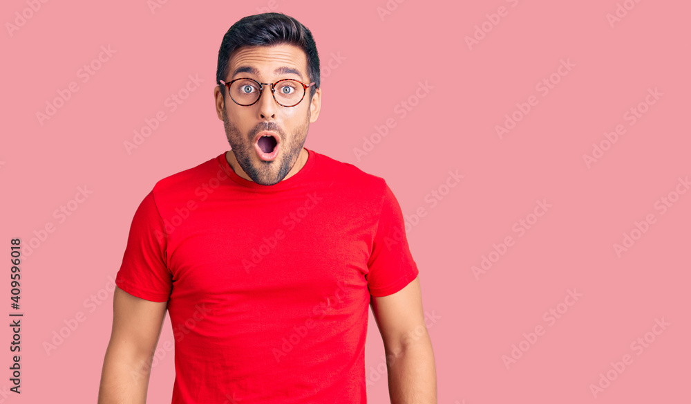Young hispanic man wearing casual clothes and glasses scared and amazed with open mouth for surprise, disbelief face - obrazy, fototapety, plakaty 