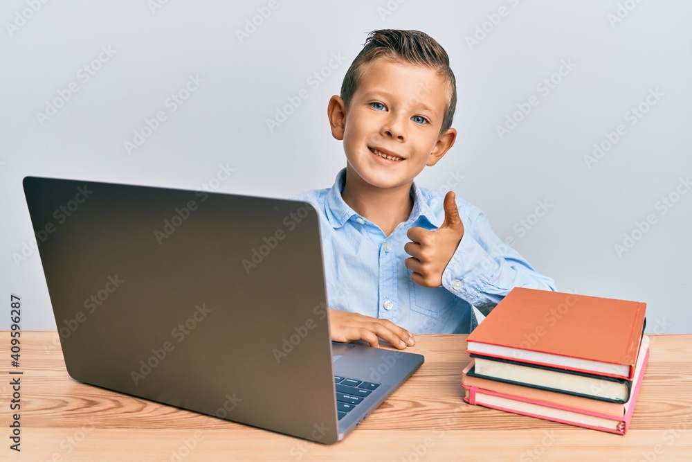 Adorable caucasian kid studying for school exam using laptop smiling happy and positive, thumb up doing excellent and approval sign Adorable caucasian kid studying for school exam using laptop smiling happy and positive, thumb up doing excellent and approval sign