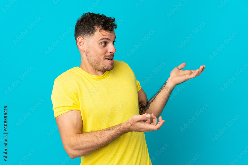 Young caucasian handsome man isolated on blue background with surprise expression while looking side